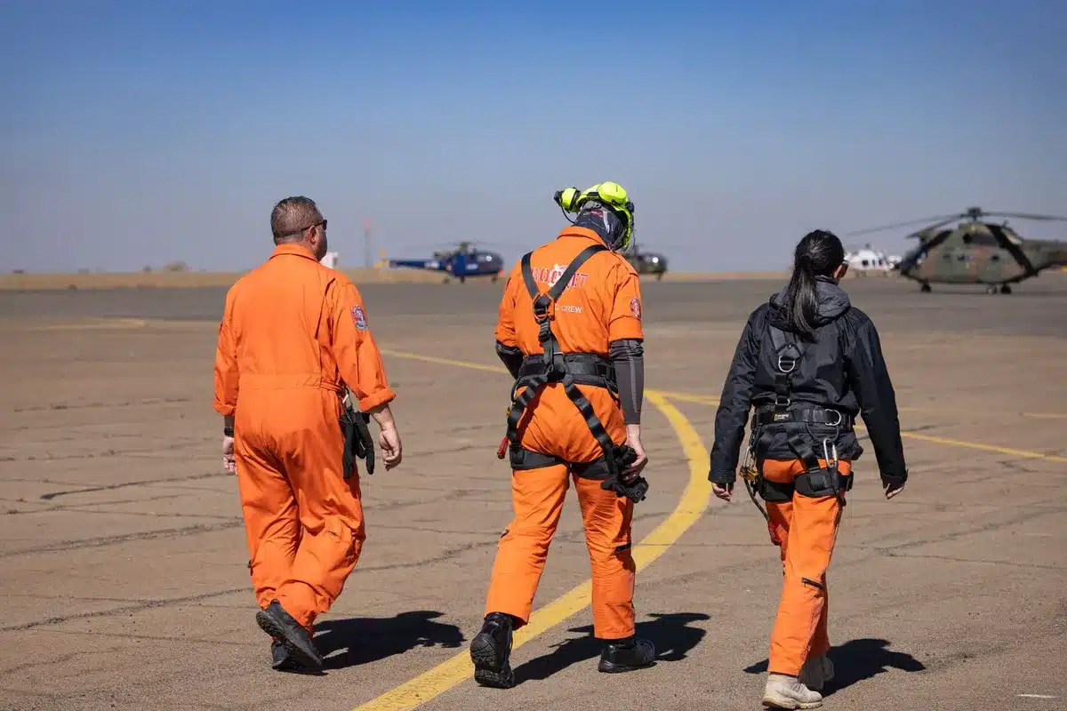A pit mine site with rescue workers and miners gathered around an excavated hole, mud-covered workers pulling bodies and equipment from the collapsed shaft, chaotic scene with dozens of people scattered across the site, urgency and tragedy visible