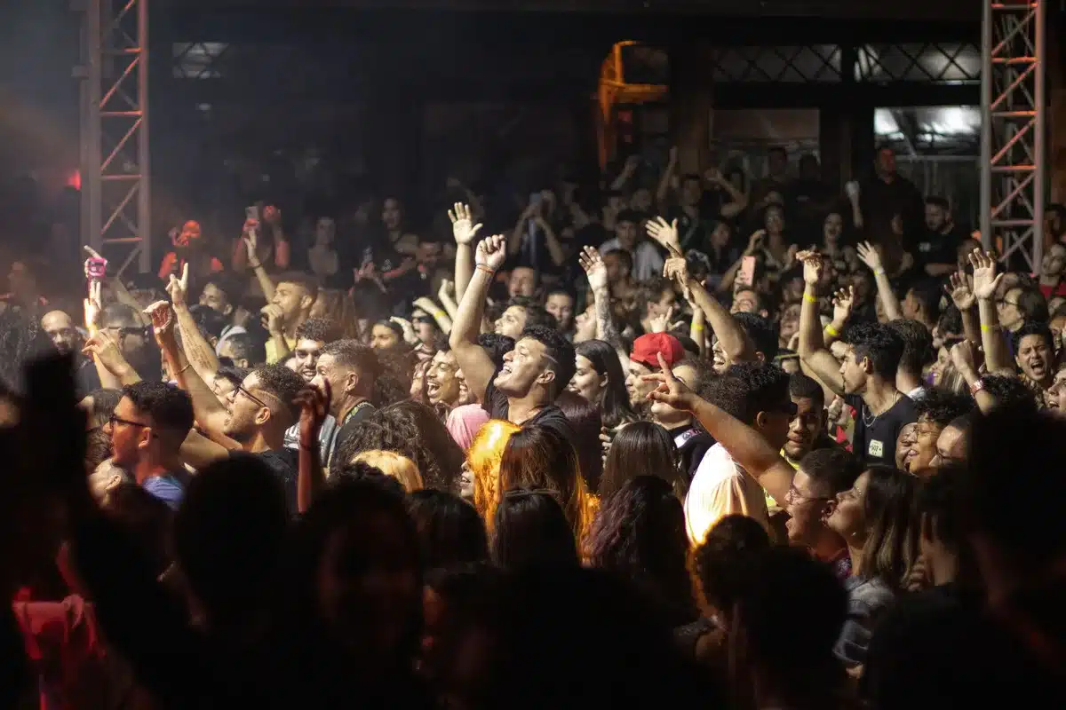 A crowded indoor venue with supporters raising their arms in celebration, confetti or streamers visible, faces blurred in the crowd.