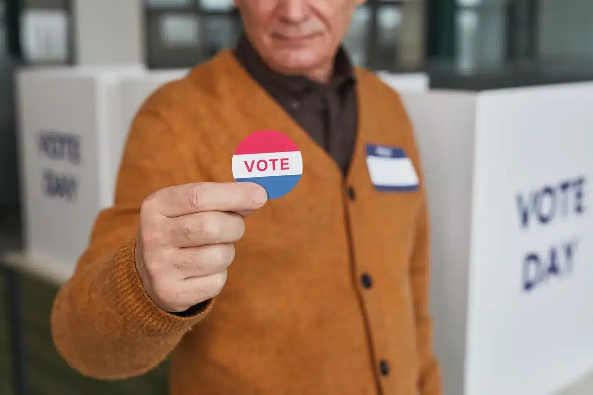 Voting booth with ballot visible, anonymous voter marking their choice, polling place interior with directional signage, democratic participation