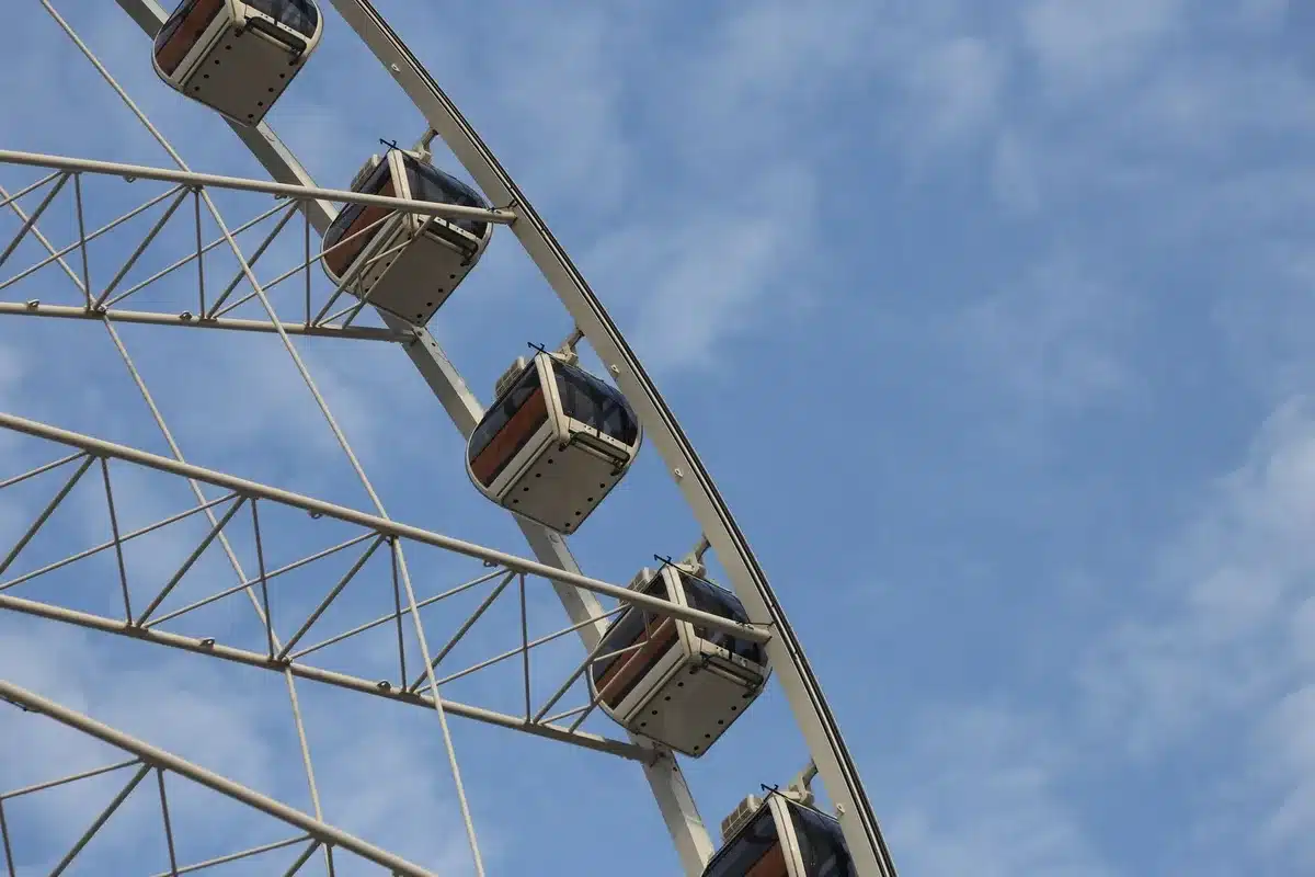 A gleaming white observation wheel rising against a clear sky, its enclosed gondolas catching sunlight, fairground landscape sprawling below, 14-mile vista visible from the apex