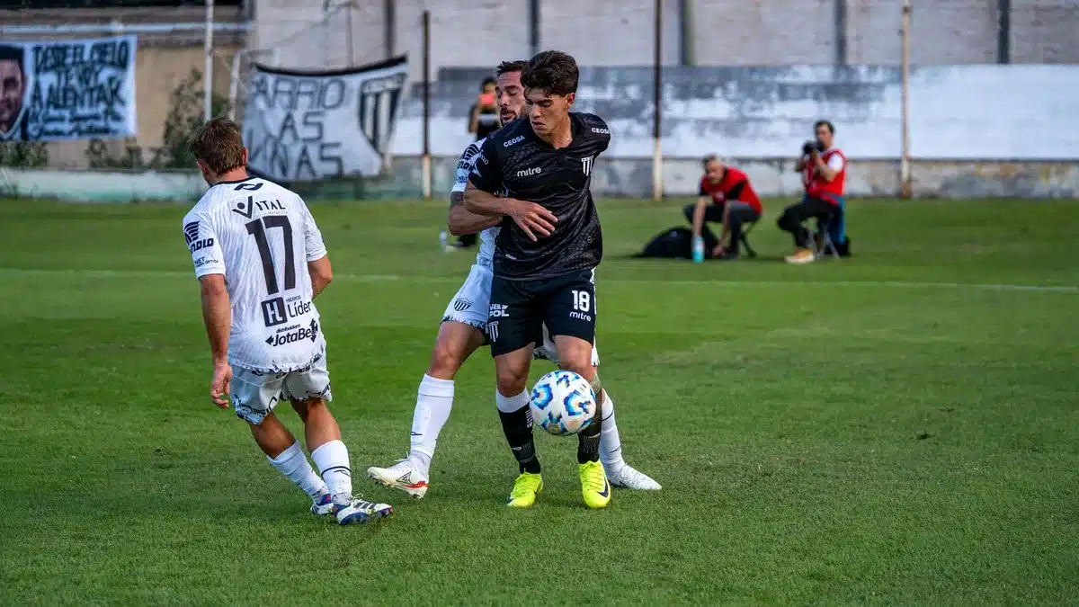 A soccer field with goal nets visible, Monterrey team colors prominent in the composition, players in formation on the pitch during a match moment, intensity and focus captured in the scene.