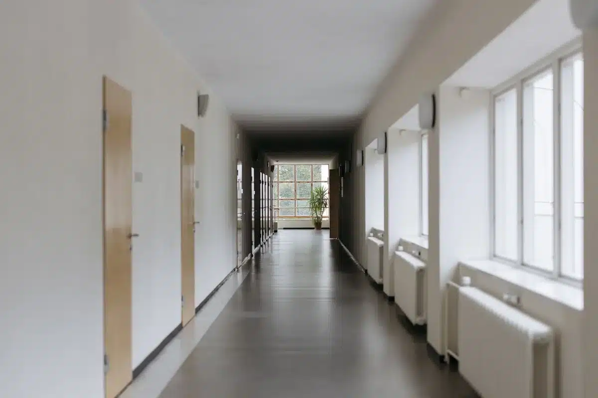 Empty courthouse hallway with wooden benches, a single briefcase on a bench, late afternoon light through tall windows, shadows stretching across the floor