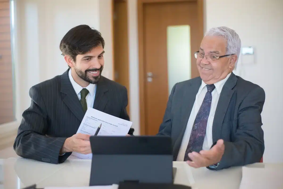 A financial advisor in a modern workspace reviewing portfolio performance on a tablet with a client seated across from them, sunlight streaming through floor-to-ceiling windows, capturing the adviser-client relationship that drives wealth management growth.
