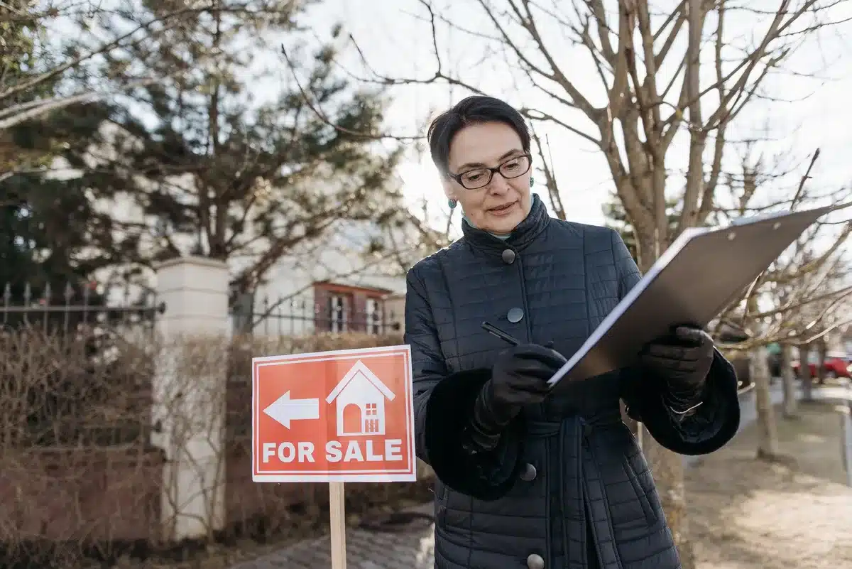 A residential home exterior with a "For Sale" sign in the front yard, photographed at dusk with soft lighting.