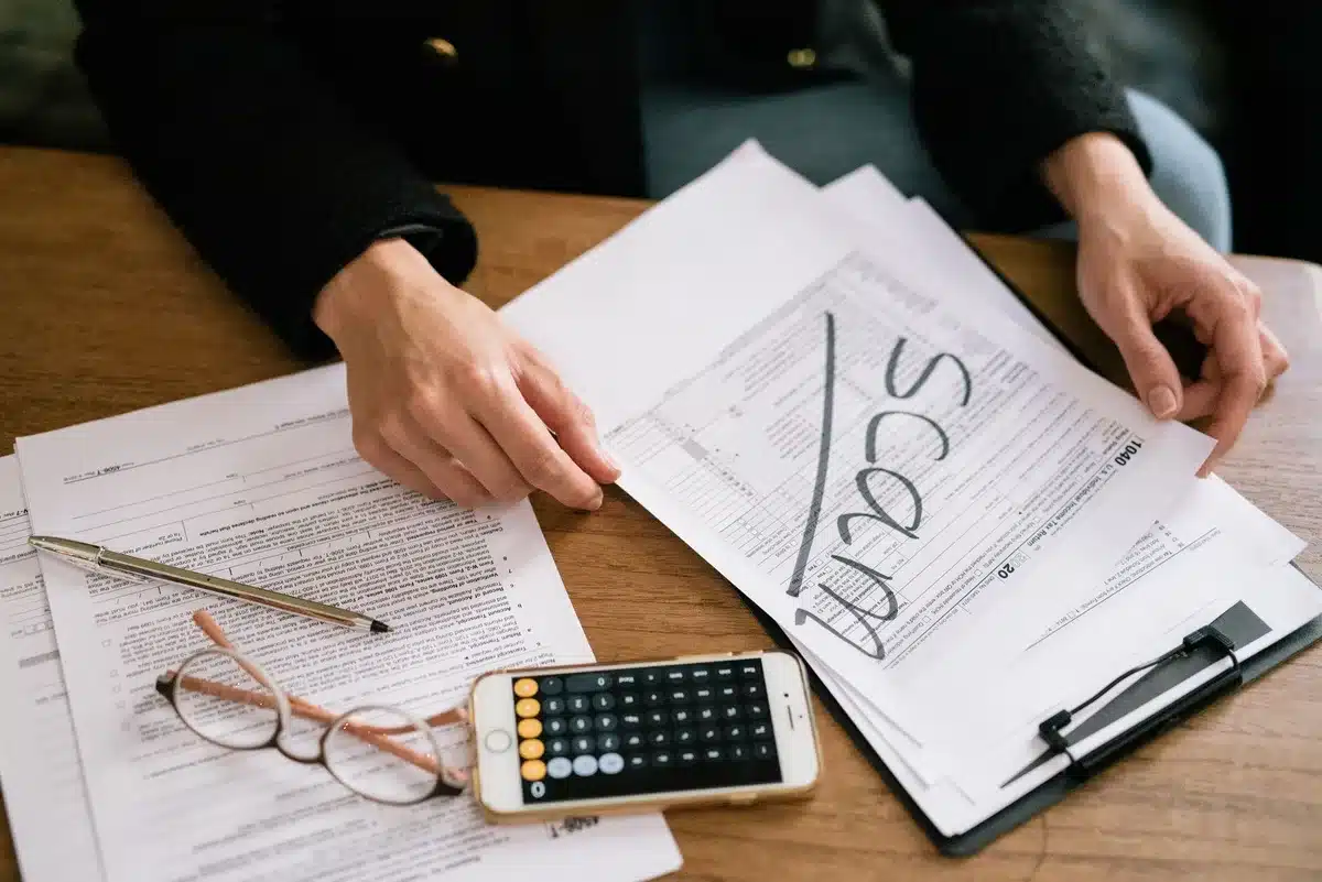 A person reviewing mortgage documents at a desk with a calculator and pen, sunlight streaming through a window, suggesting careful financial planning.