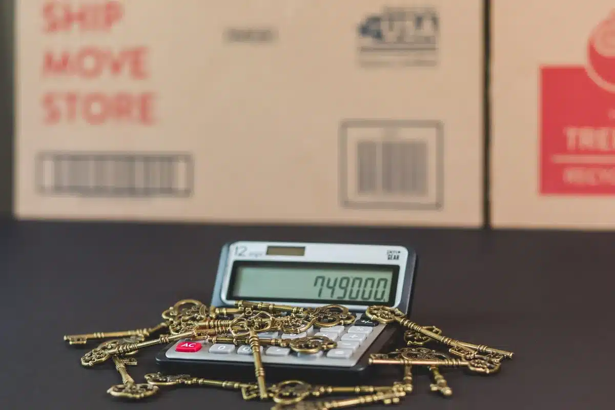 A calculator, mortgage documents, and a pen on a desk with financial charts visible in the background.