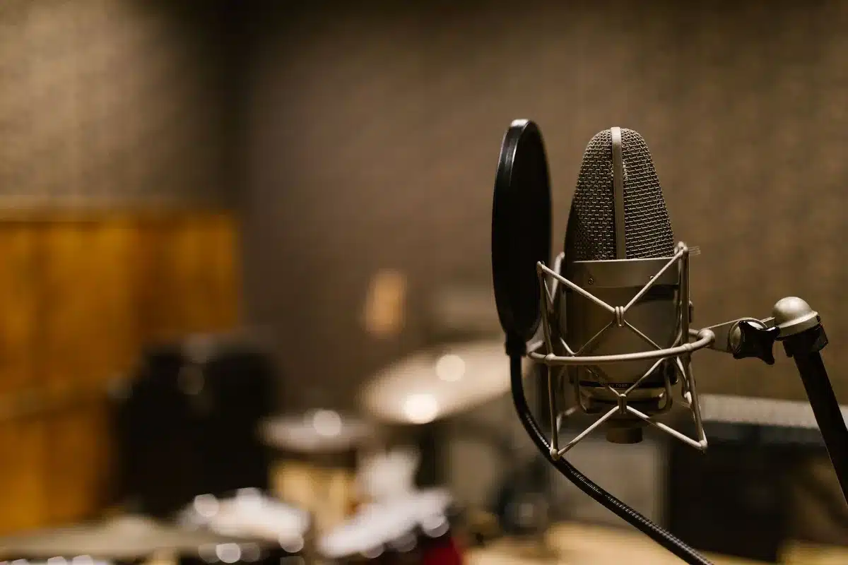 A microphone on a dimly lit studio stand with a coiled cable trailing into shadow, dust particles visible in a harsh spotlight beam.
