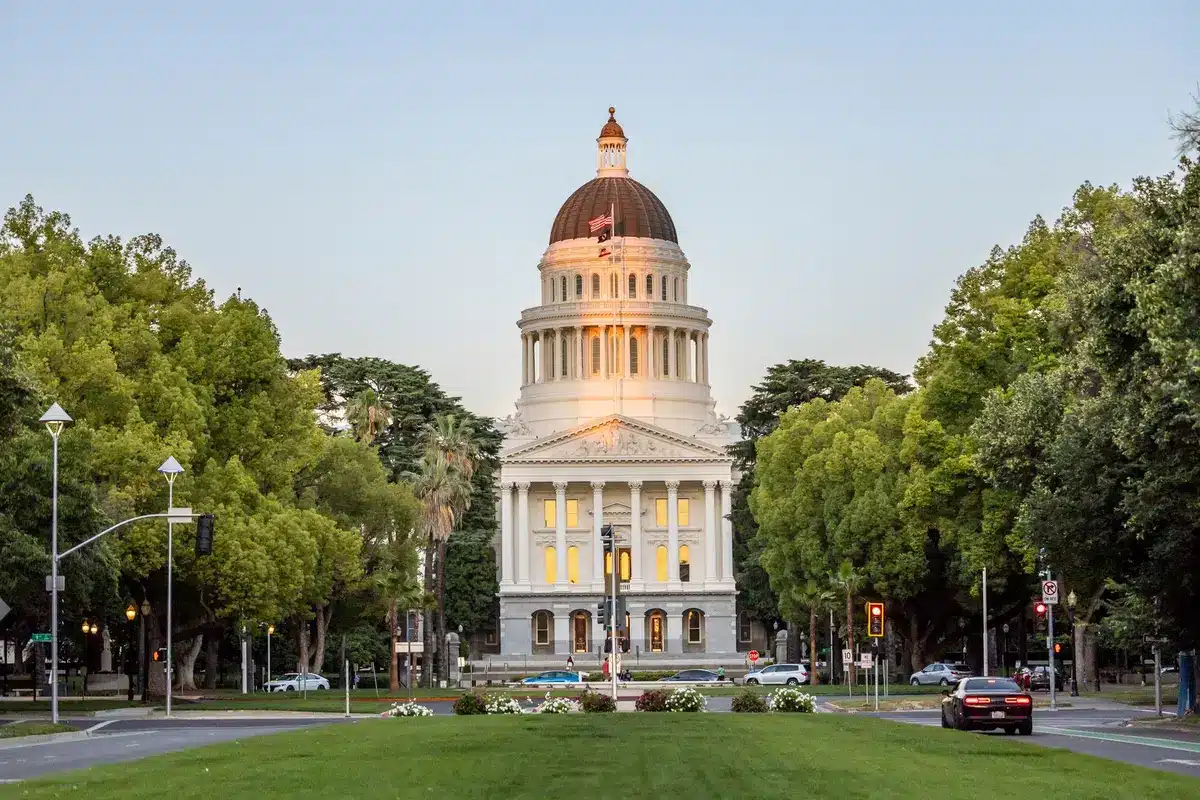 A Michigan state capitol building exterior with a pride flag visible, architectural detail, morning light, empty plaza