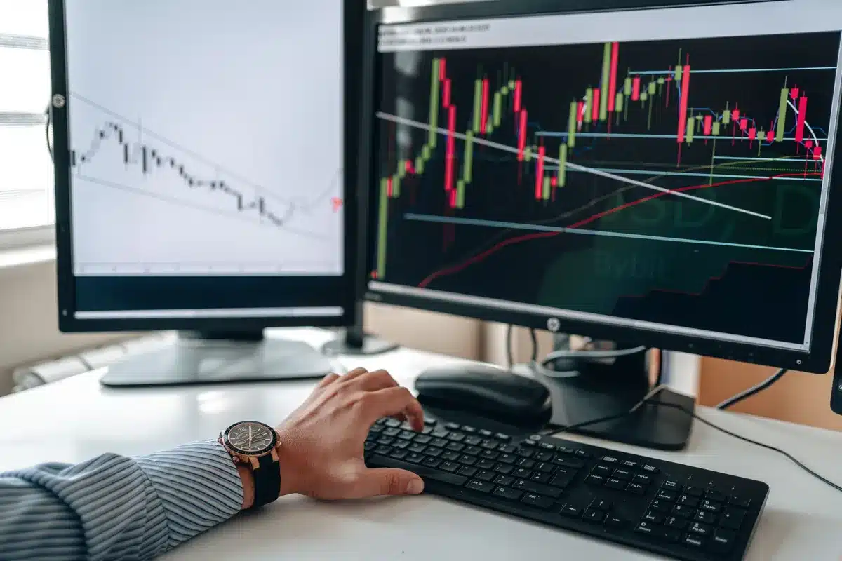 A close-up of a financial advisor's desk with a computer monitor displaying stock recommendation data, research documents, and notes scattered around, showing the analytical work behind stock selection.