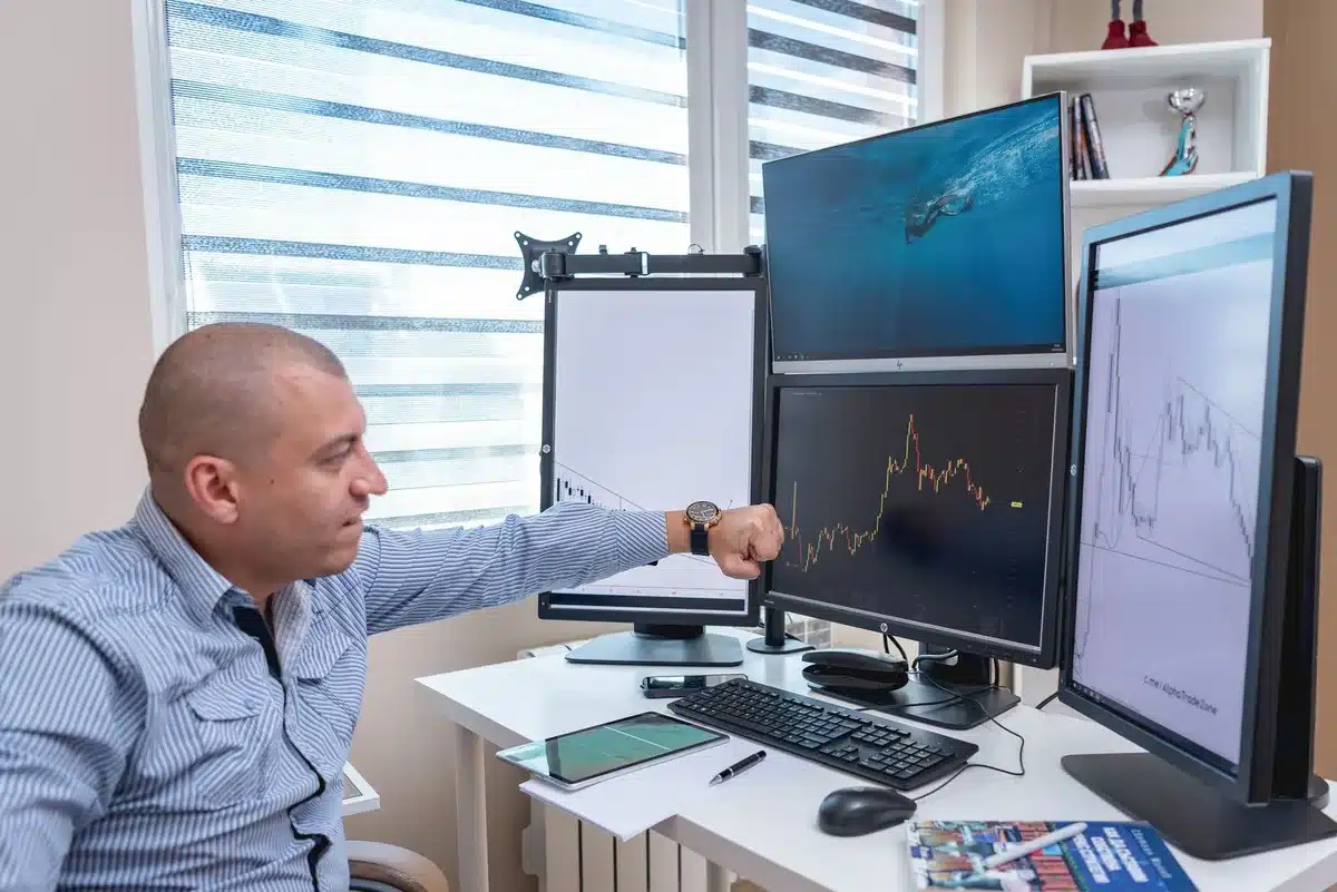 A financial advisor's desk with a computer monitor displaying stock recommendation data, research documents, and analysis notes scattered around, showing the analytical work behind stock selection.
