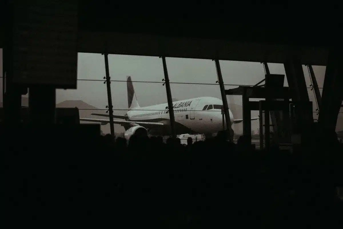 An airport tarmac with aircraft lined up at gates, some with boarding doors open, ground crew standing idle, overcast afternoon light casting long shadows, a sense of suspended activity and delay