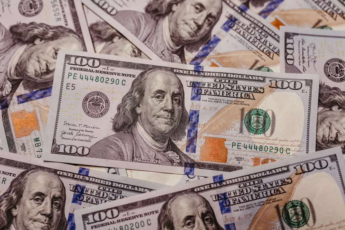 A stack of U.S. dollar bills beside a Bitcoin coin, both under harsh spotlight, with the dollar bills appearing more prominent, symbolizing the shift from crypto focus to cash reserves