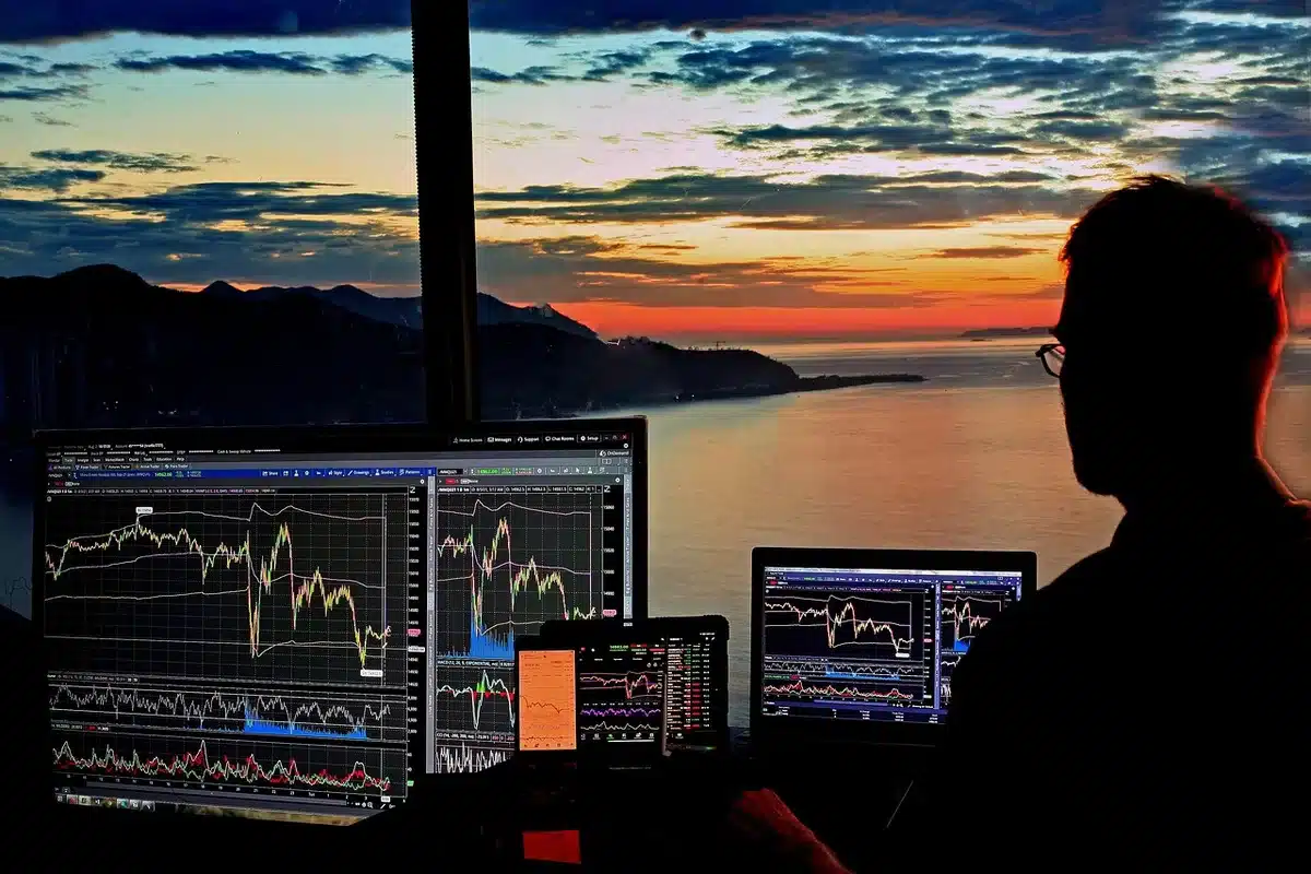 Glowing stock market ticker displaying red numbers and downward arrows on a dark screen, oil price chart climbing sharply beside it