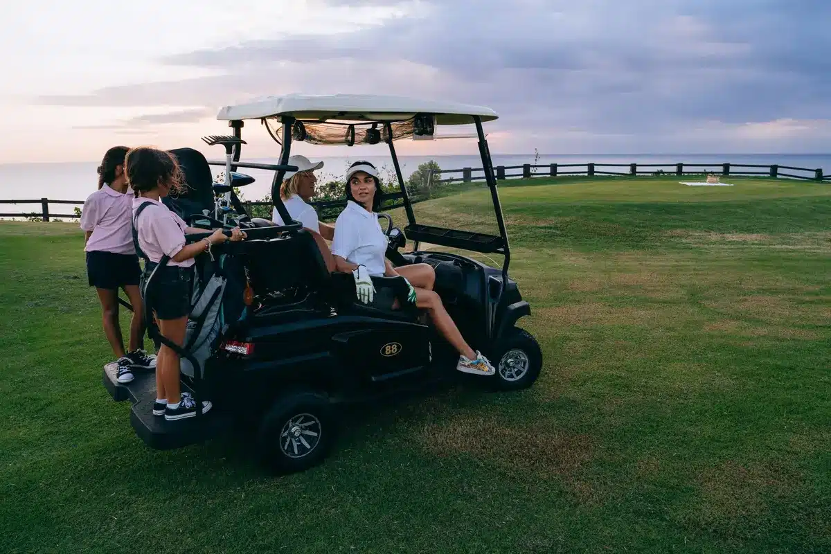 A golf course setting at dawn, manicured fairways stretching into morning mist, a golf cart parked on the green, a laptop bag visible in the background, the clubhouse silhouetted against the sky