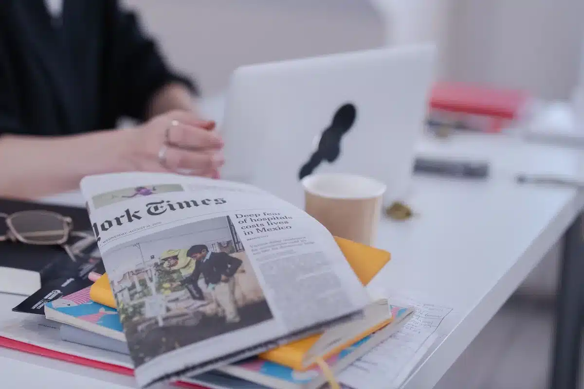 A laptop screen glowing with bright news headlines and positive social media feeds, hands poised above a keyboard, a coffee cup and notepad beside it, soft office lighting reflecting off the screen