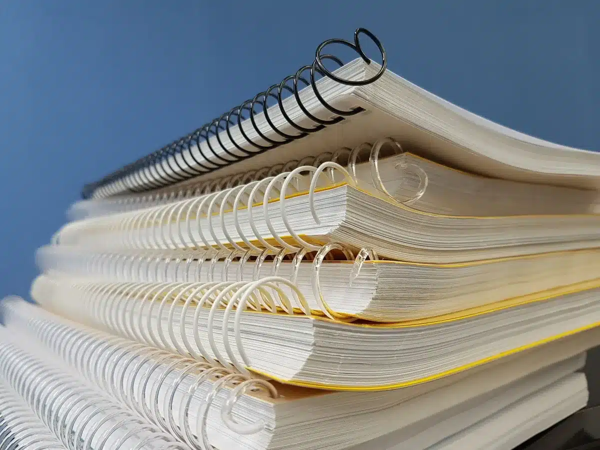 Printed documents stacked on a desk, a hand holding a page, office lighting, close-up detail, neutral tones