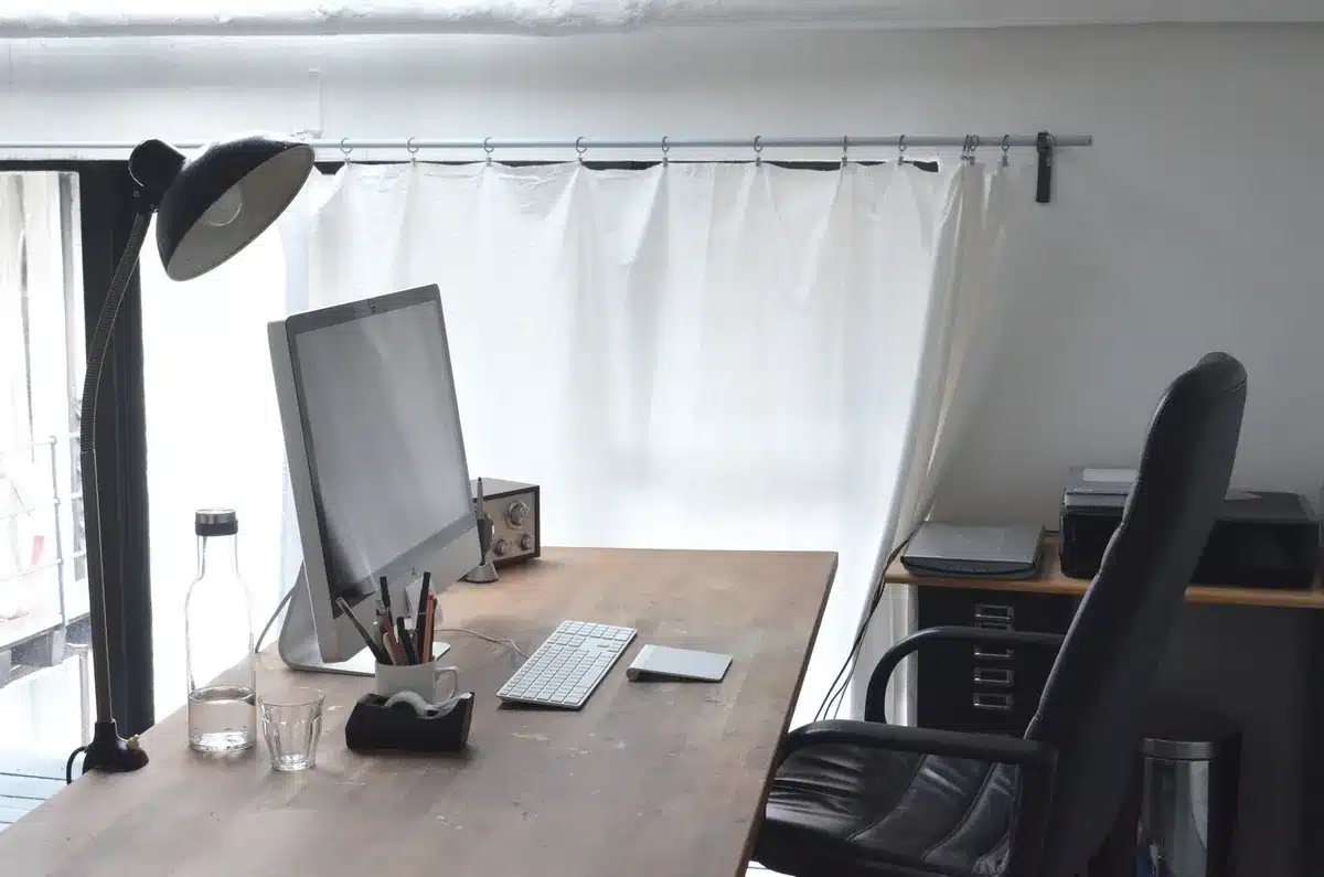 A modest office setting with documents and papers on a desk, a portable printer visible, morning light through windows, suggesting behind-the-scenes White House work.