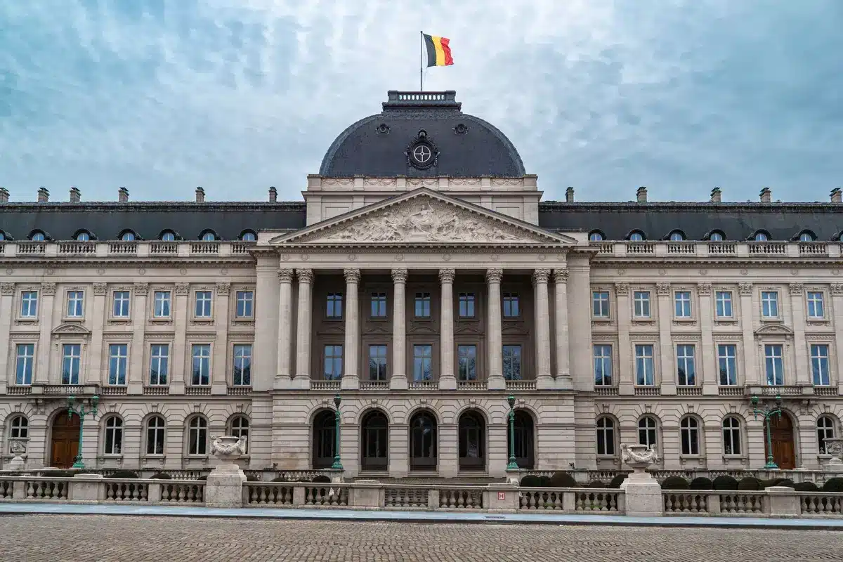 A formal government building facade with a flag at half-mast against grey skies, representing diplomatic tension between nations