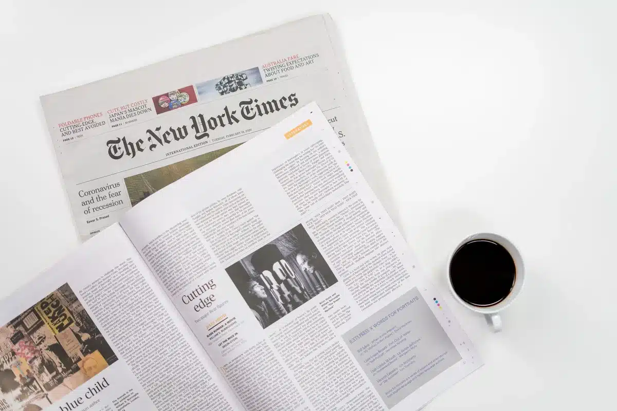A financial newspaper spread with stock market data and company logos visible, a pen resting on highlighted articles, natural daylight illuminating the page