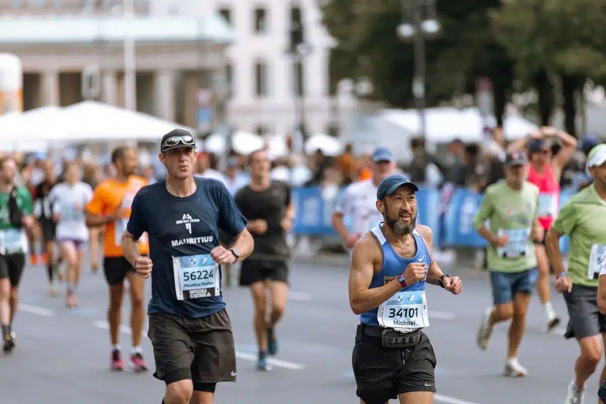 Marathon runners in motion along a city street, silhouettes catching golden light, anonymous participants mid-stride with focused determination