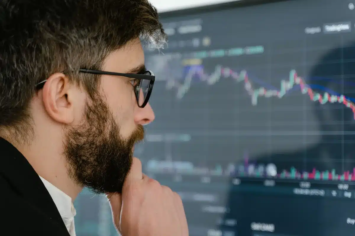 A glowing stock ticker displaying semiconductor company symbols and ascending price charts, candlestick patterns in sharp focus, blue and green digital numerals reflecting on glass, a dim trading floor in soft background blur