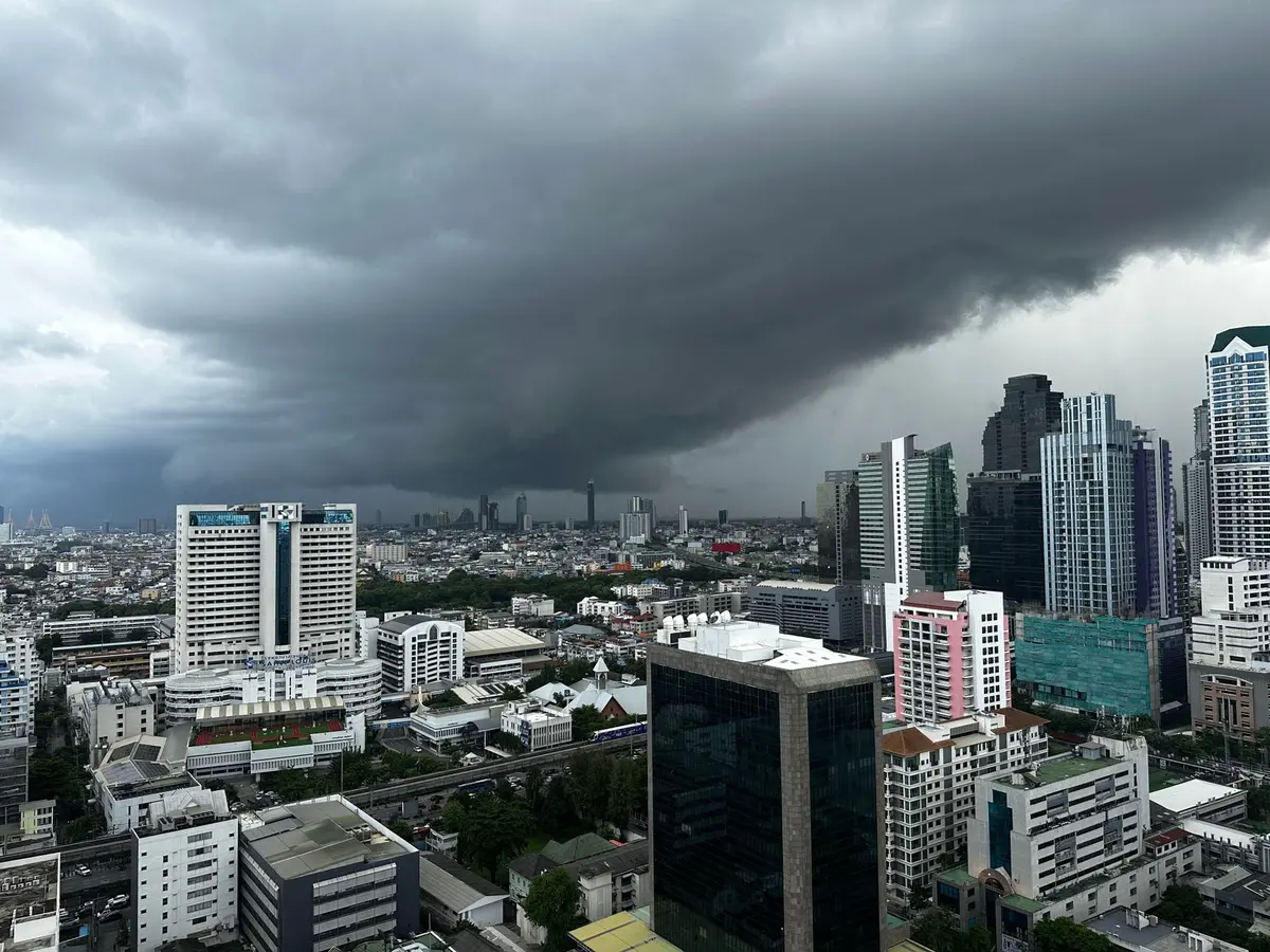 Towering dark cumulonimbus clouds building over an urban skyline, lightning branching across the sky, rain curtains visible in the distance, street lights reflecting off wet pavement