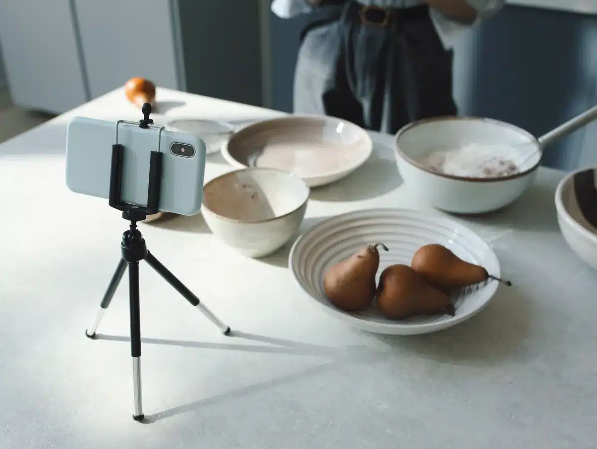 A split-screen view of modern recipe content: left side shows traditional printed recipe cards with handwritten notes, right side shows a glowing tablet displaying a video cooking tutorial with vibrant food imagery, contrast between analog and digital