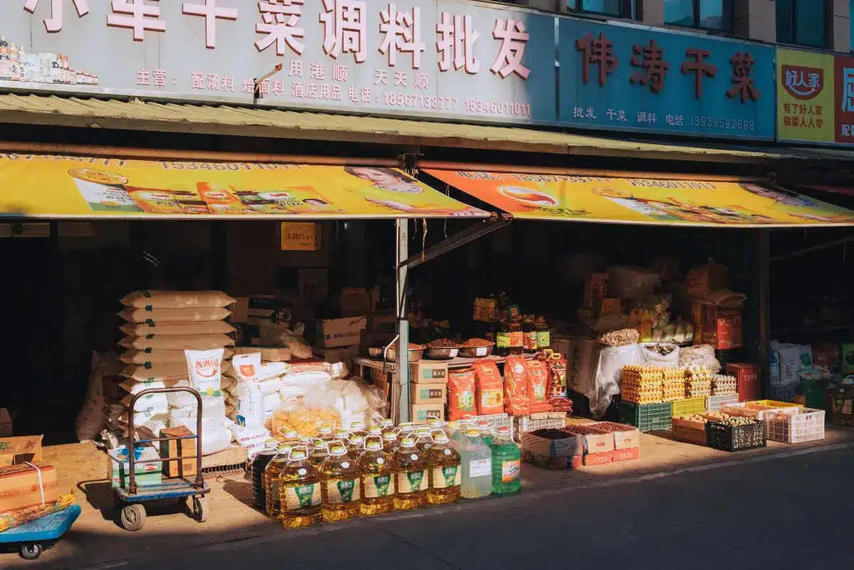 A family-owned grocery storefront with distinctive signage, neighborhood location, warm interior lighting visible through windows, fresh produce displays in the entrance, a sense of community gathering place