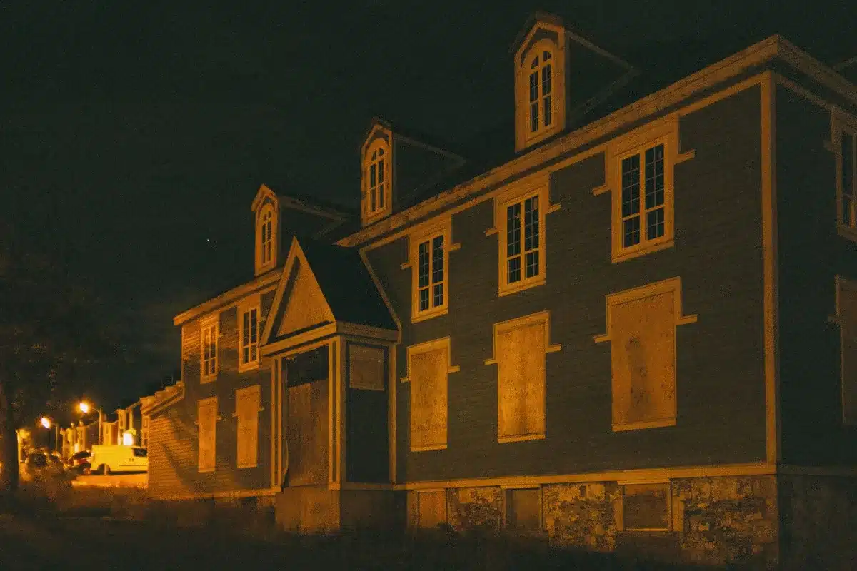 Empty public housing complex at dusk, weathered brick facade, boarded windows, bare courtyard with a single lamp post, overcast sky, sense of urban neglect