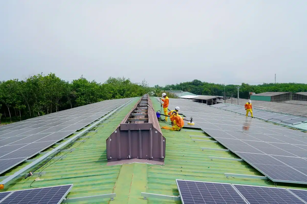 Construction workers in safety gear installing solar panels on a public housing rooftop, blue sky, morning light, collaborative energy