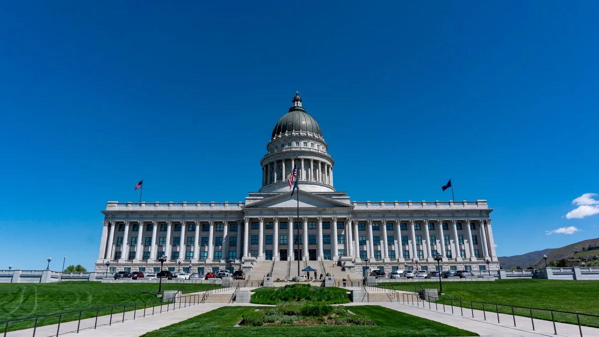 State capitol building exterior with flag at half-staff, voting booth partially visible through window