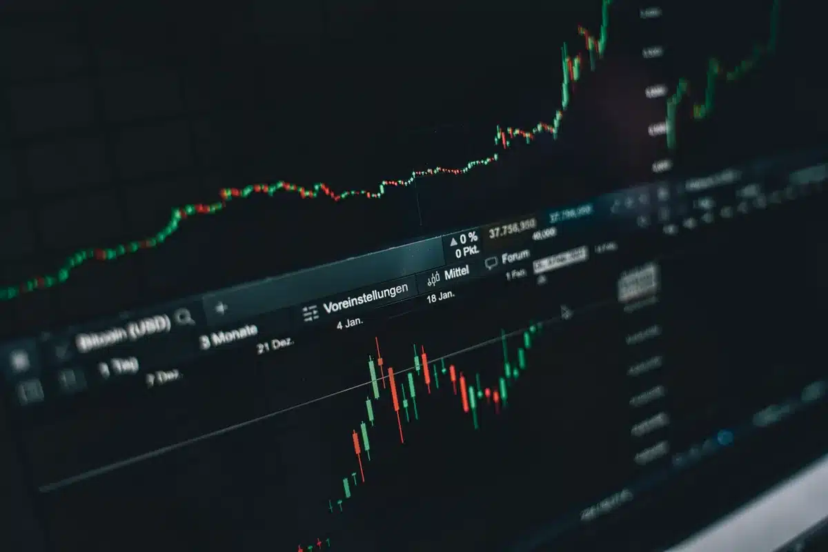 Oil price chart declining on a trading screen, candlestick bars in red, financial data streaming below, trading floor lights reflected in glass