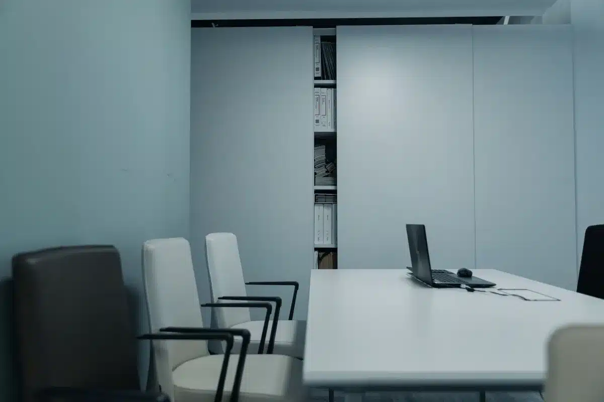 A corporate office corridor with empty desks and chairs in dim light, filing cabinets lining the walls, a single desk lamp casting a lone glow, sense of organizational transition
