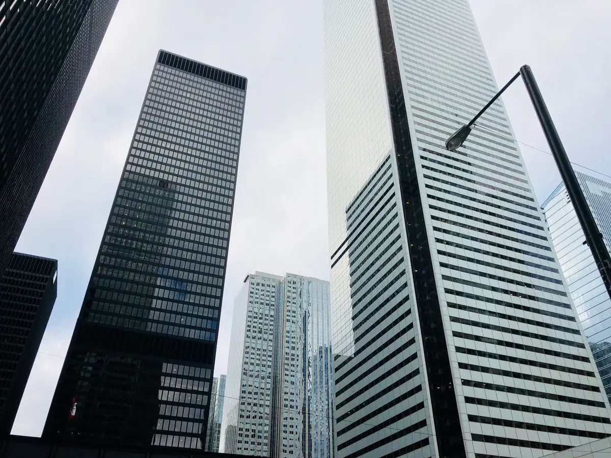 Manhattan skyline with financial district buildings reflecting in glass, abstract representation of wealth and corporate power, cool blue tones, no identifying landmarks or logos