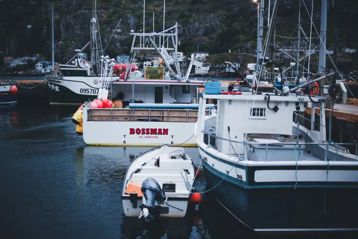 A weathered fishing boat docked at an Alaskan harbor at dusk, with mountains in the background, evoking the natural resource and outdoor heritage central to Alaska's identity