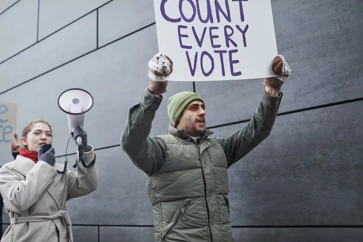 A crowd of supporters at a political rally or election night event, with anonymous silhouettes and raised arms showing collective emotion. Lighting and energy suggest a campaign celebration.