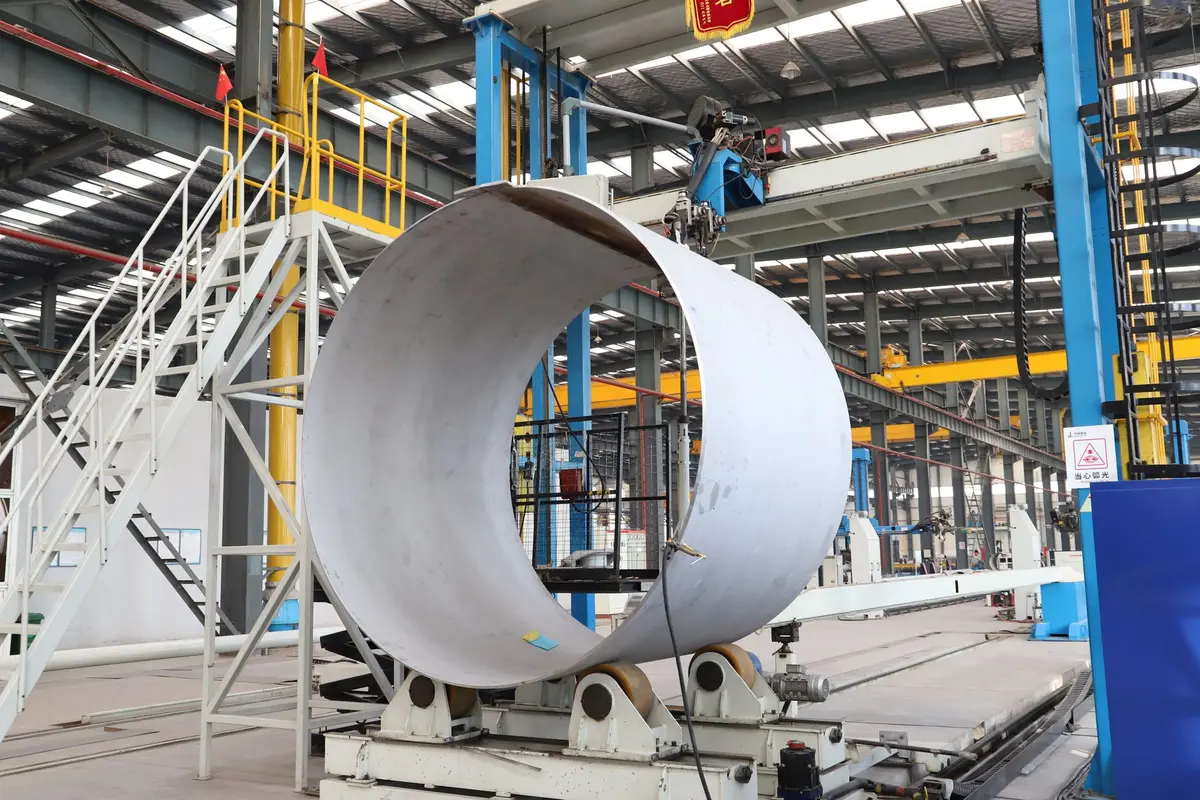 Manufacturing floor showing transformer coil winding equipment and workers assembling large electrical components in an industrial facility.