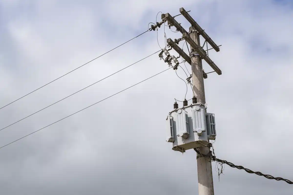 Close-up of an industrial electrical transformer mounted on a utility pole, weathered and showing age, against an overcast sky.