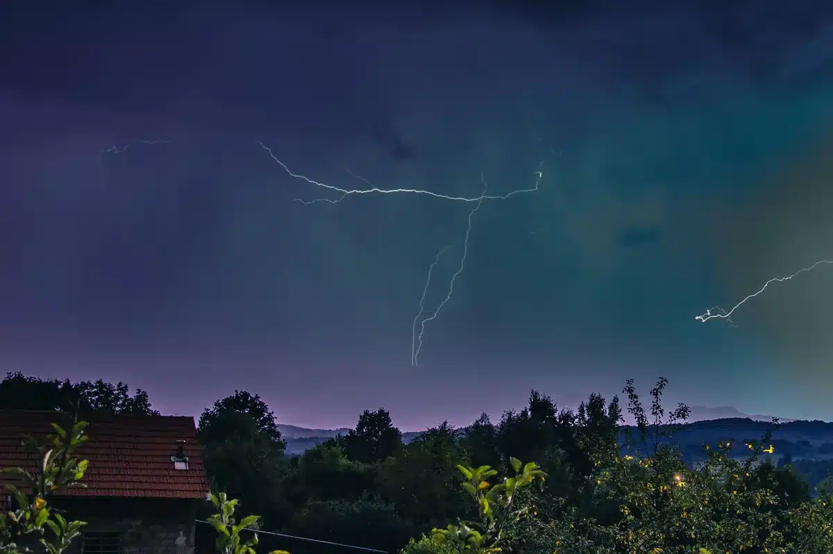 Dark storm clouds gathering over a city skyline with lightning branching across the sky, heavy rain falling, power lines silhouetted against the dramatic weather