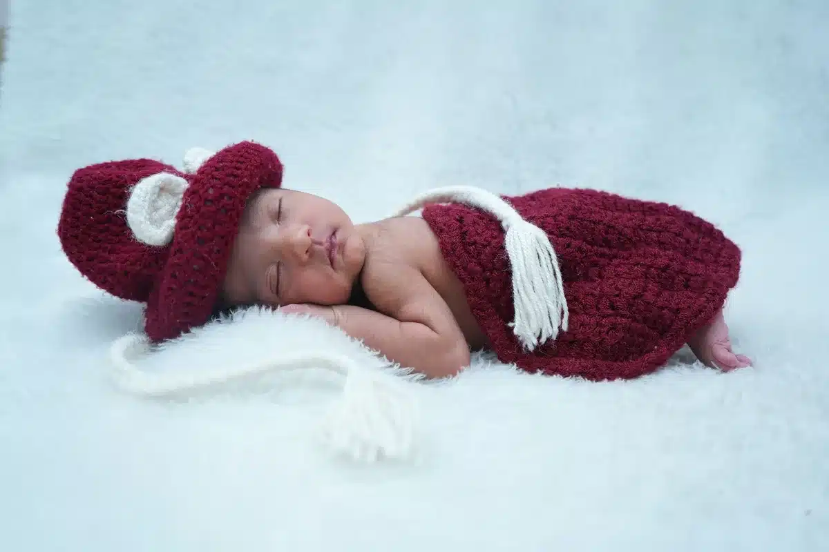 A newborn baby wrapped in soft hospital blankets, tiny hand visible, peaceful sleeping expression in warm, gentle lighting.