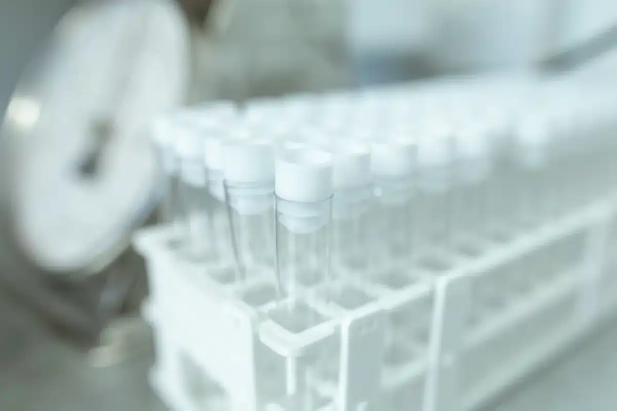 A large-scale pharmaceutical manufacturing facility floor with rows of production equipment, quality control stations, and regulatory compliance signage visible, conveying the scale and complexity of modern drug production.