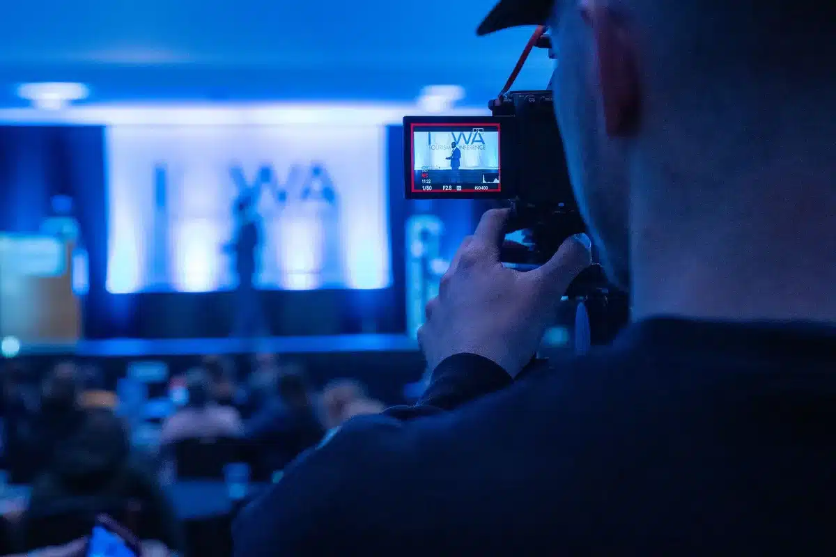 Debate stage with podiums and audience seating in a neutral venue, dim lighting casting shadows across empty chairs, a single microphone catching light