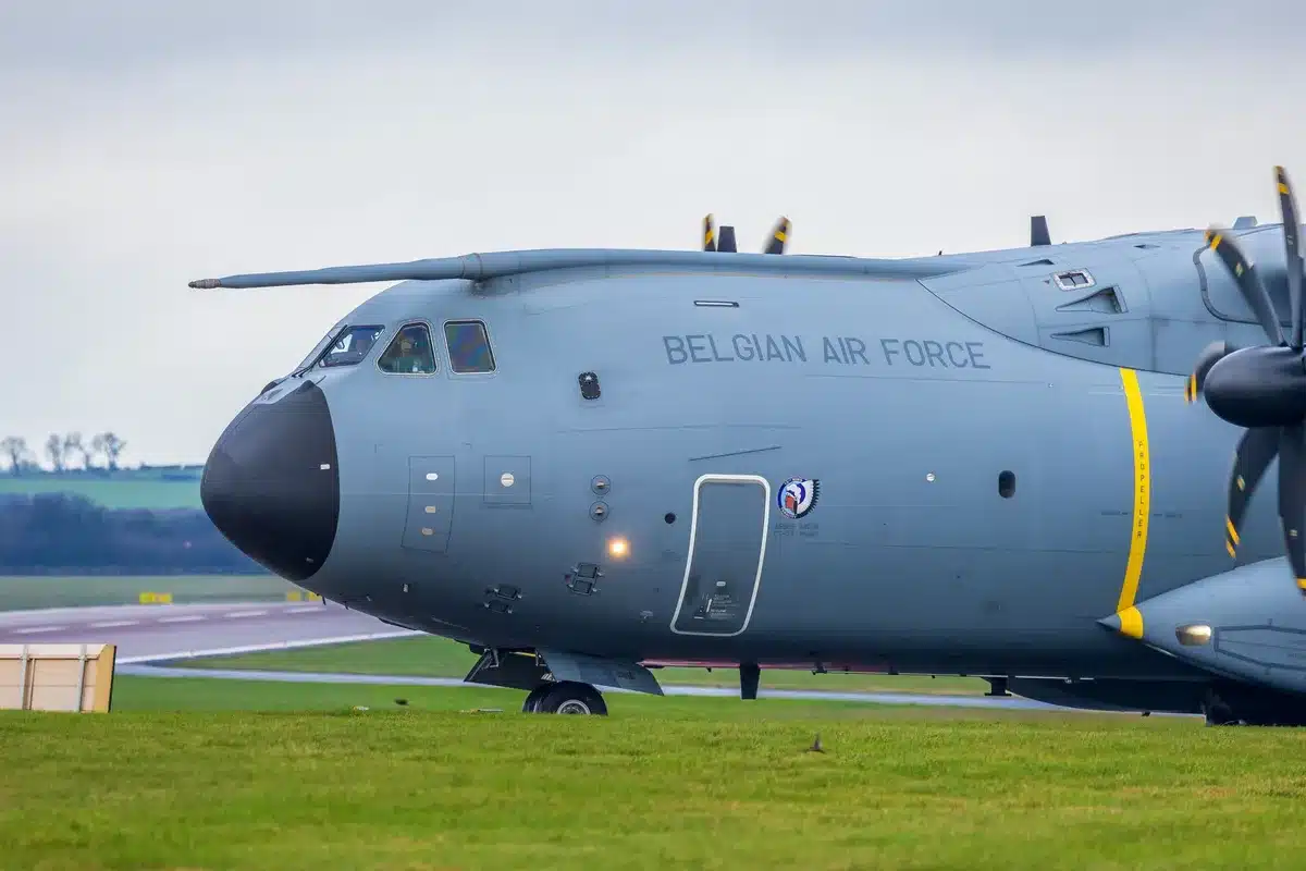 A military cargo aircraft on a tarmac at an international airport, diplomatic security personnel visible in the foreground, tension evident in the scene