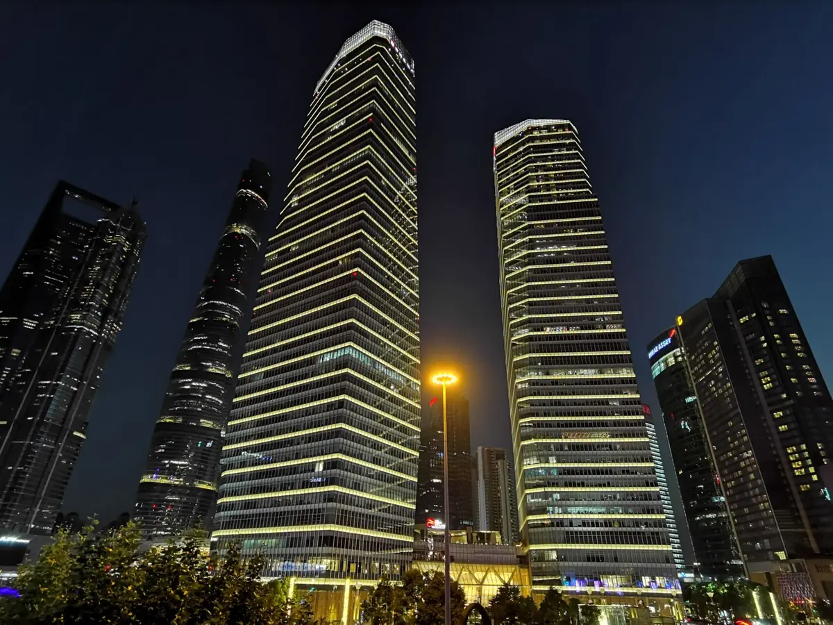 A lone figure standing in an empty financial district plaza at dusk, skyscrapers looming in shadow, a stock ticker display flickering in the distance, economic uncertainty palpable