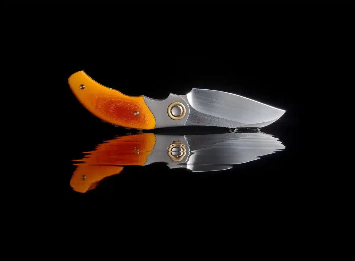 A karambit knife twirling in close-up under dim amber light, the blade catching a reflection, shadows of two figures tense and motionless in the background.