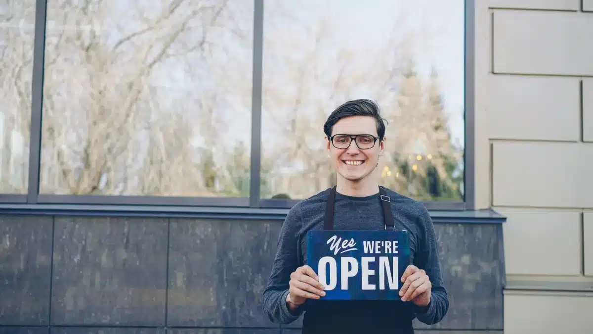 A small-business owner standing in an office or storefront setting, focused and determined, with campaign materials or community spaces visible in the background, representing grassroots political engagement.