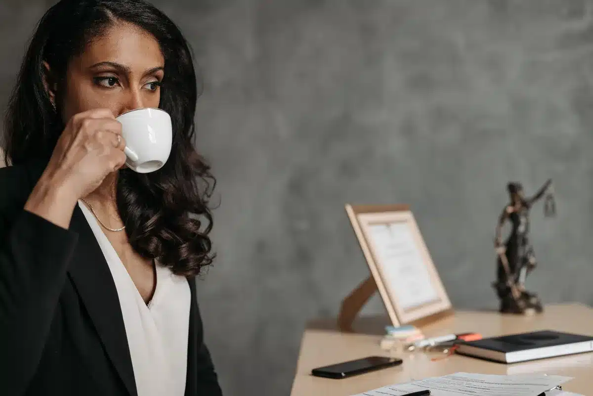 Professional in a corporate office setting, desk with legal documents and a computer monitor, natural light from windows, focused and composed expression, neutral business environment