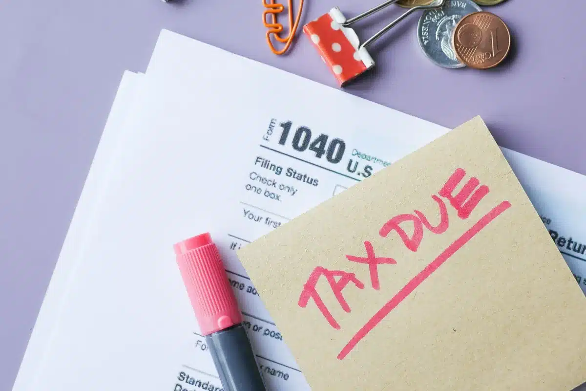 A stack of tax forms and financial documents spread across a surface, with a calculator and pen nearby; soft lighting emphasizes the complexity and volume of paperwork