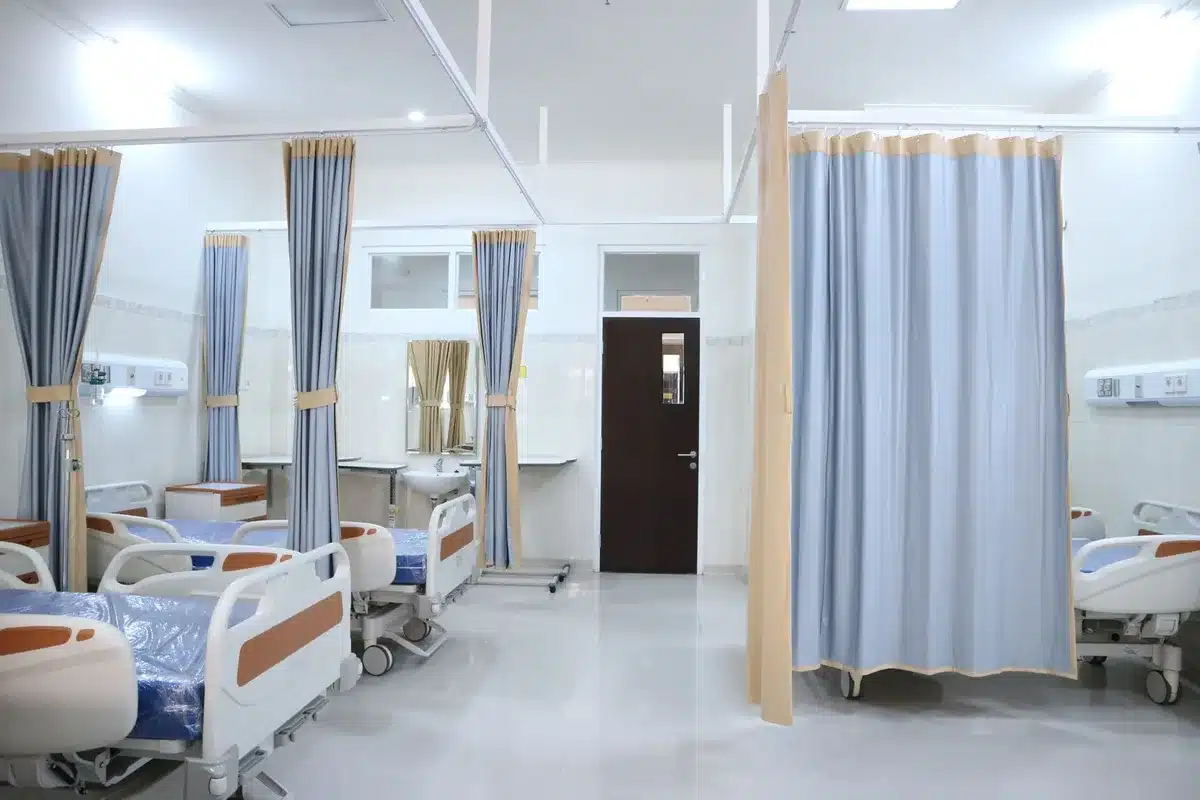 A modern clinic interior with examination rooms and medical equipment, fluorescent lighting illuminating sterile white walls and patient care stations, representing expanded health center infrastructure