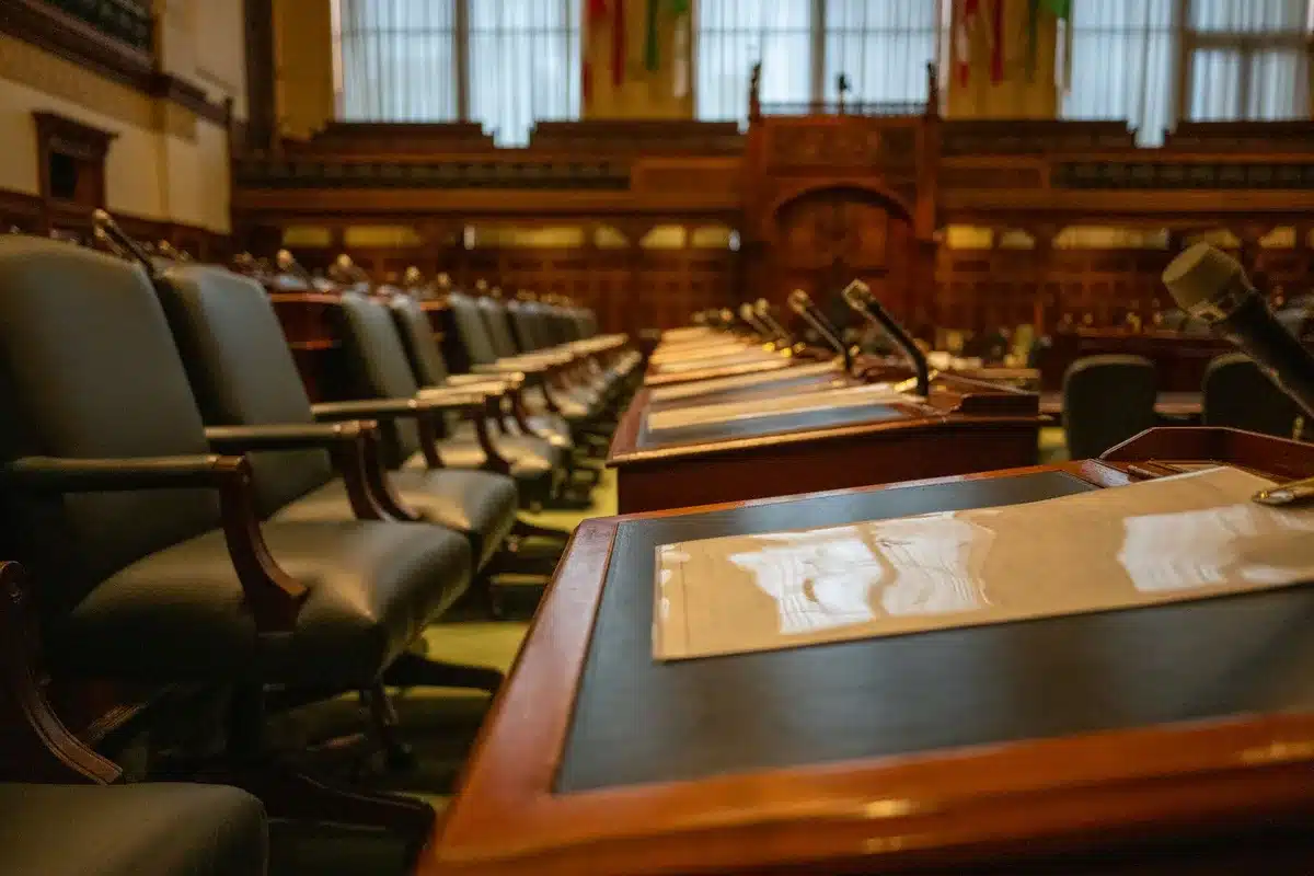 A sparse government office with an empty desk and chair facing a window overlooking a city, suggesting absence or vacancy in leadership.